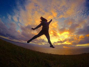 Woman jumping over sea against sky during sunset