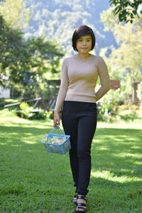 Full length portrait of woman holding basket while standing on grass