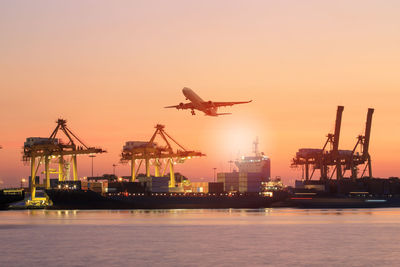 Cranes at commercial dock against sky during sunset