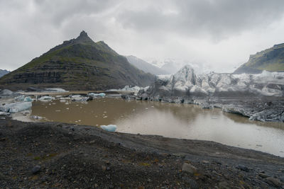 Ice floating in muddy waters of glacier lake with glacier in background on a cloudy and rainy day.