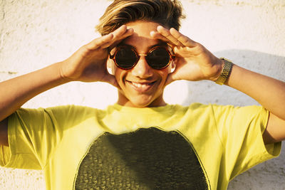 Portrait of smiling teenage boy wearing sunglasses against wall