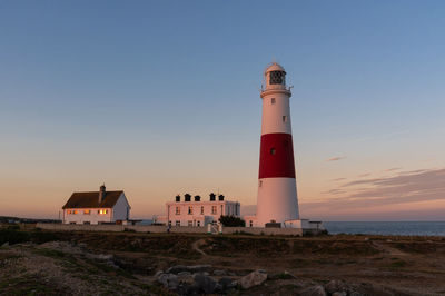 Lighthouse by sea against sky during sunset