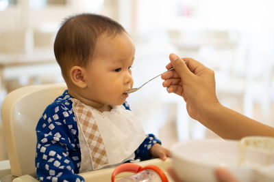 Cropped hands of mother feeding food to daughter sitting on high chair at home