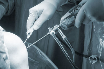 Midsection of doctors performing surgery on patient knee with equipment
