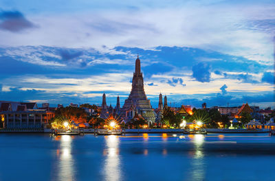 Illuminated buildings by river against sky