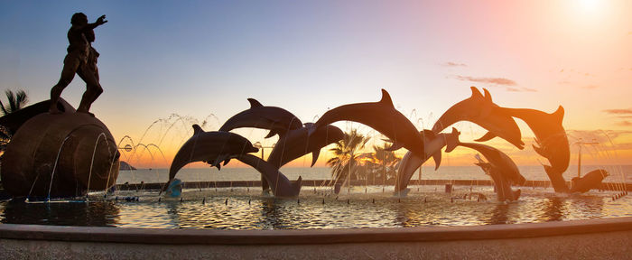 People on shore against sky during sunset