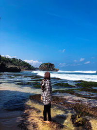 Rear view of woman standing at beach against sky