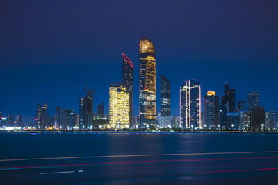 Illuminated modern buildings in city by river at night