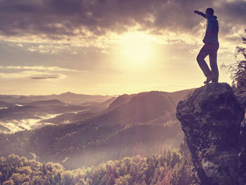 Hiker climbed on rock above foggy valley. hrensko range. man watch over valley to bright morning sun