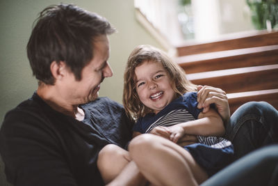 Portrait of happy daughter with smiling father sitting on steps at home