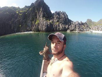 Portrait of shirtless man in sea against mountains