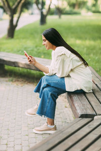 A girl writes sms messages or uses applications on a smartphone while sitting on a bench in the park