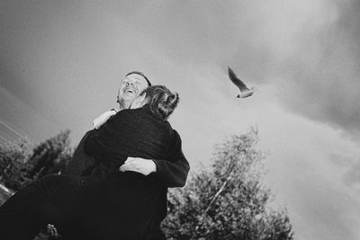 Man lifting girlfriend against sky