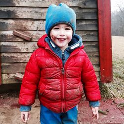 Portrait of cute boy standing on field against wooden wall during winter