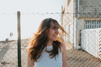 Young woman standing against chainlink fence