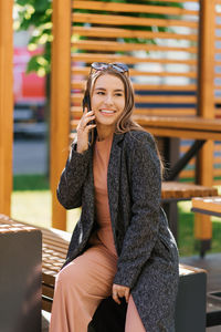 Young woman is talking on the phone, sitting on a city bench