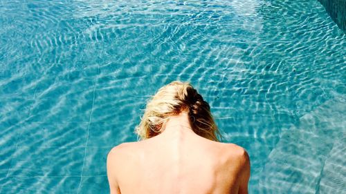 High angle view of naked woman sitting at poolside on sunny day