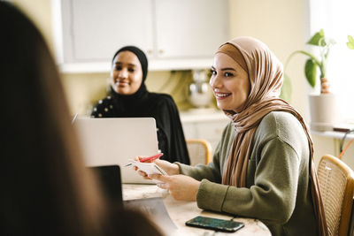 Smiling young woman in hijab studying with friends at home