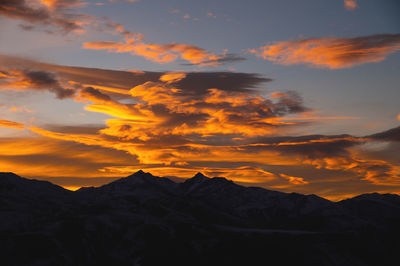 Sunset in the mountains, mountain silhouette against a cloudy sky in orange colors