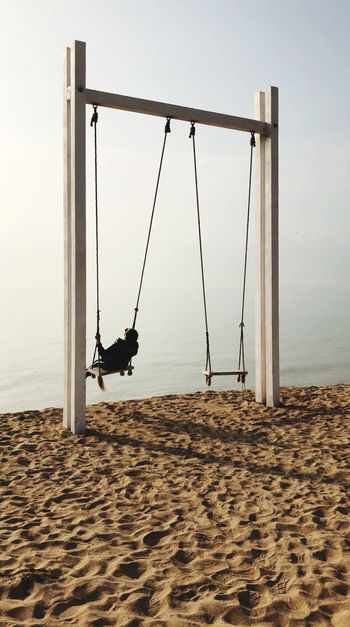 Rear view of mature woman swinging at sandy beach