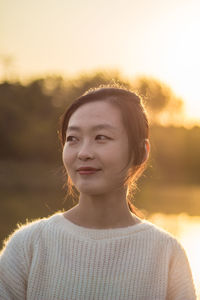 Thoughtful young woman standing against lake during sunset