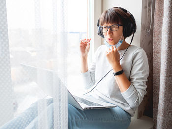 Woman in medical mask remote works from home. she speaks online with somebody on laptop. quarantine.