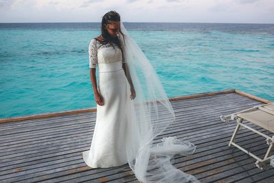 Bride standing on floorboard over sea against sky