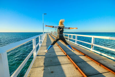 Full length of excited woman jumping on pier by sea against sky