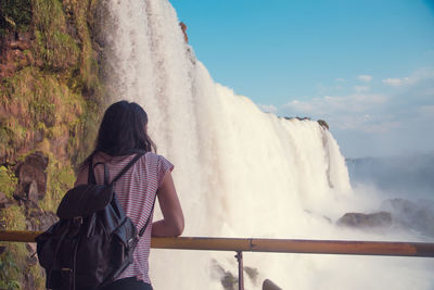 Rear view of woman with backpack standing by waterfall