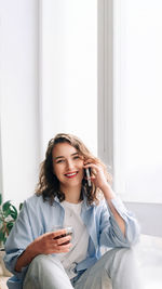 Young woman using mobile phone while sitting on bed at home