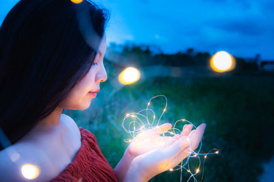 Close-up of beautiful woman holding illuminated lighting equipment at night