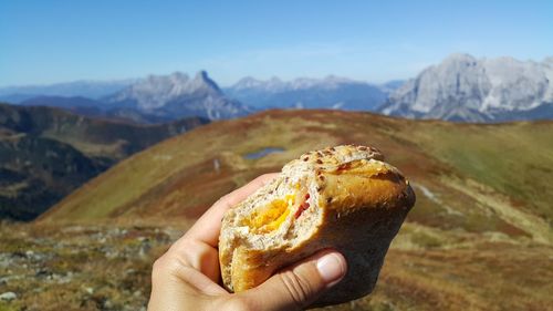 Cropped hand holding burger against mountain