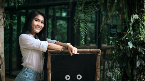 Portrait of smiling young woman standing against trees