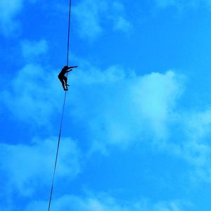 Low angle view of man on rope against blue sky