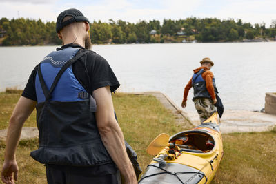 Rear view of men carrying kayak at coast