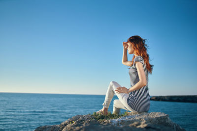 Woman sitting by sea against clear sky