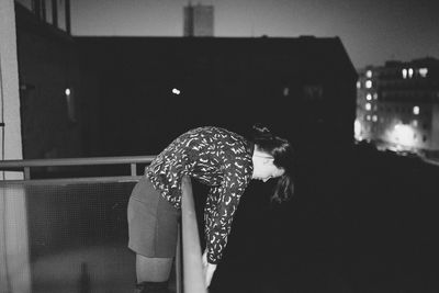 Side view of woman bending over railing at night