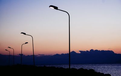 Silhouette street light by sea against sky during sunset