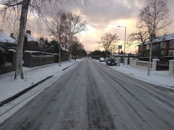 Snow covered road against sky during sunset