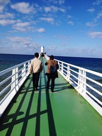 Rear view of people walking on pier over sea against sky