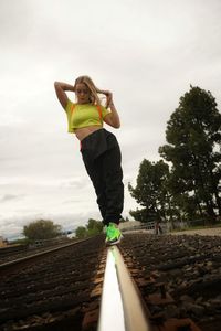 Midsection of woman standing by railroad tracks against sky