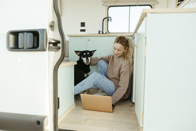 Happy young freelancer using laptop with dog in motor home