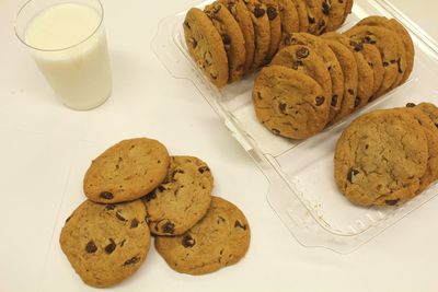 High angle view of chocolate chip cookies by milk on white table