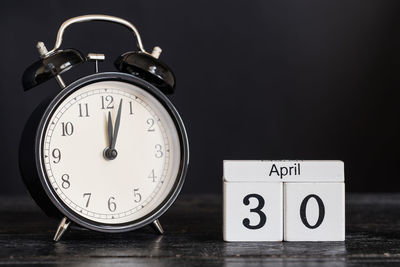 Close-up of clock with calendar on table against black background