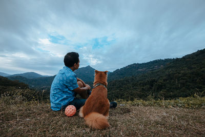 Rear view of man with dog sitting on land against sky
