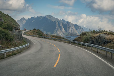 Empty road leading towards mountains against sky