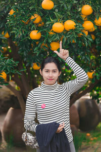 Portrait of woman standing pointing at oranges growing on tree