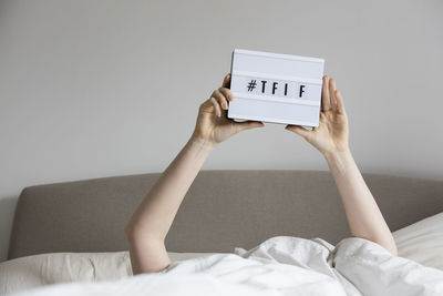 Midsection of woman holding hands on bed against wall at home