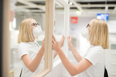 Side view of woman wearing mask standing by mirror at store