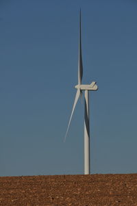 Low angle view of wind turbines on field against clear blue sky